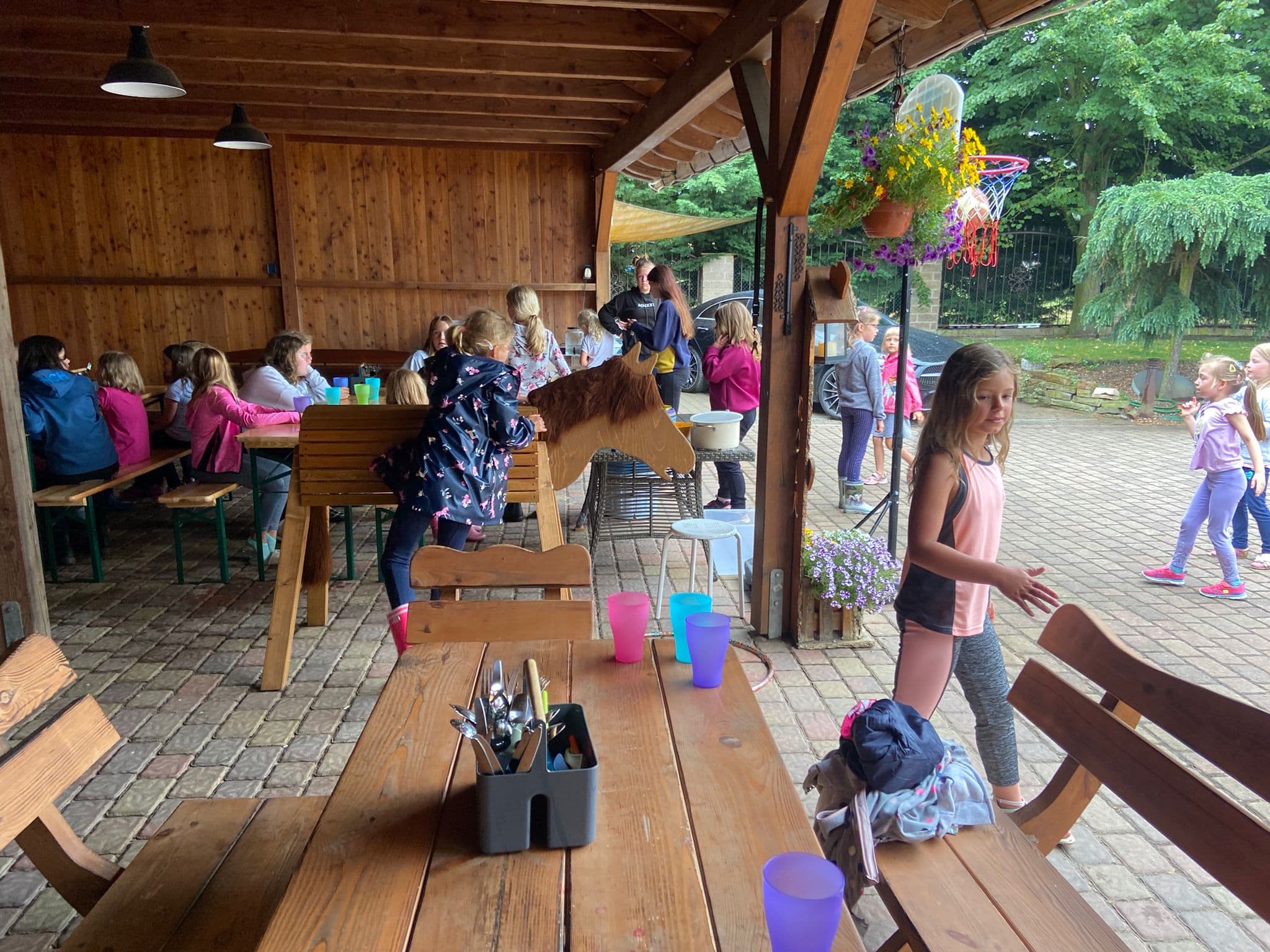 Überdachter Sitzplatz mit langen Holztischen, an denen Kinder essen